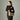 Woman wearing a beige leather shoulder bag with chain strap, styled with a fitted brown dress against a neutral background