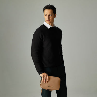 Man wearing a black sweater holding a tan leather clutch bag in hand