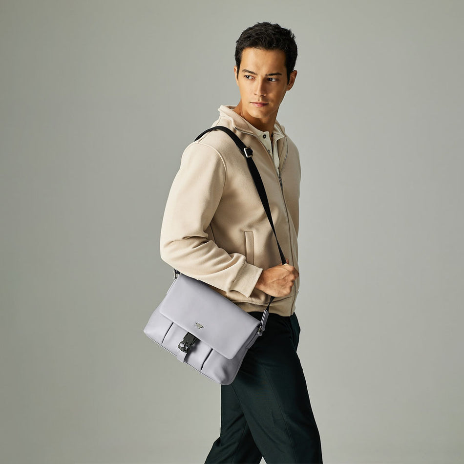 Man wearing a beige hoodie with a light grey leather crossbody messenger bag over the shoulder