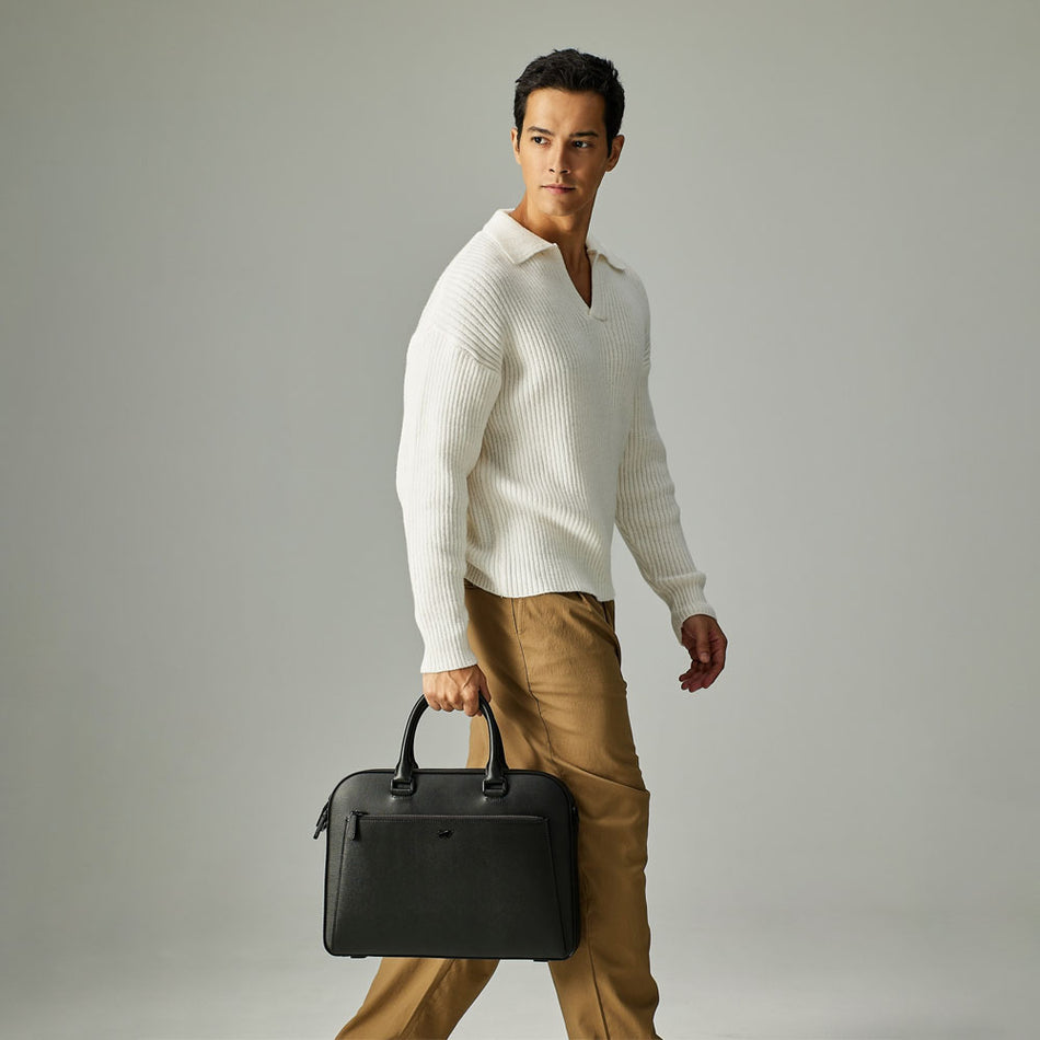 Male model carrying a black Braun Büffel leather briefcase, styled with a white knit top and brown trousers